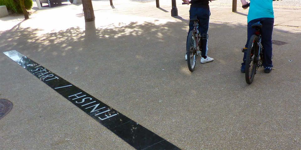 A photograph showing the back of two children on BMX bikes with a crude black start and finish line on a concrete road floor.