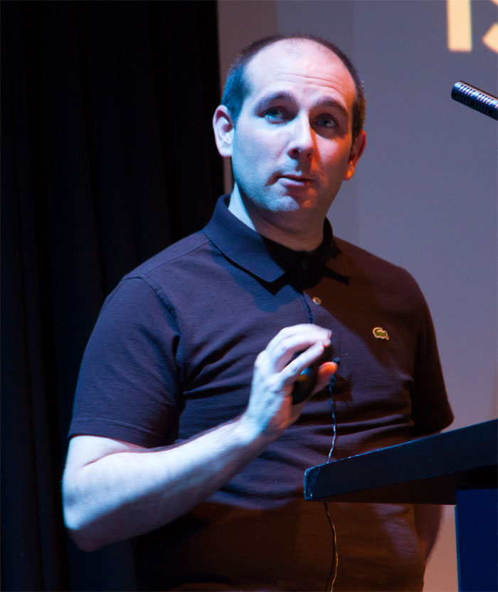 A photo of Sam speaking holding his presentation clicker.