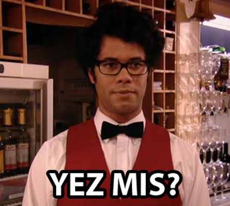 A photo of Moss from The IT Crowd in a scene where he’s dressed as a barman saying Yes Miss?